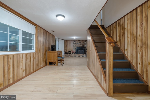 stairway with a textured ceiling, wooden walls, hardwood / wood-style floors, and a wood stove