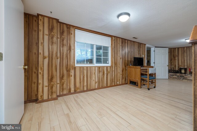 interior space featuring a textured ceiling, light wood-type flooring, and wood walls