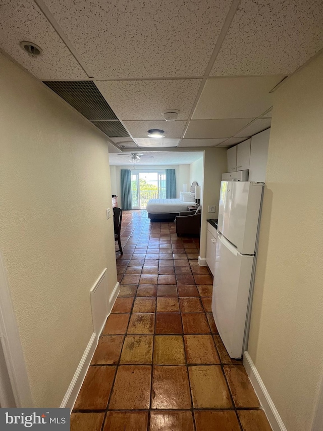 hallway with a drop ceiling and dark tile patterned flooring