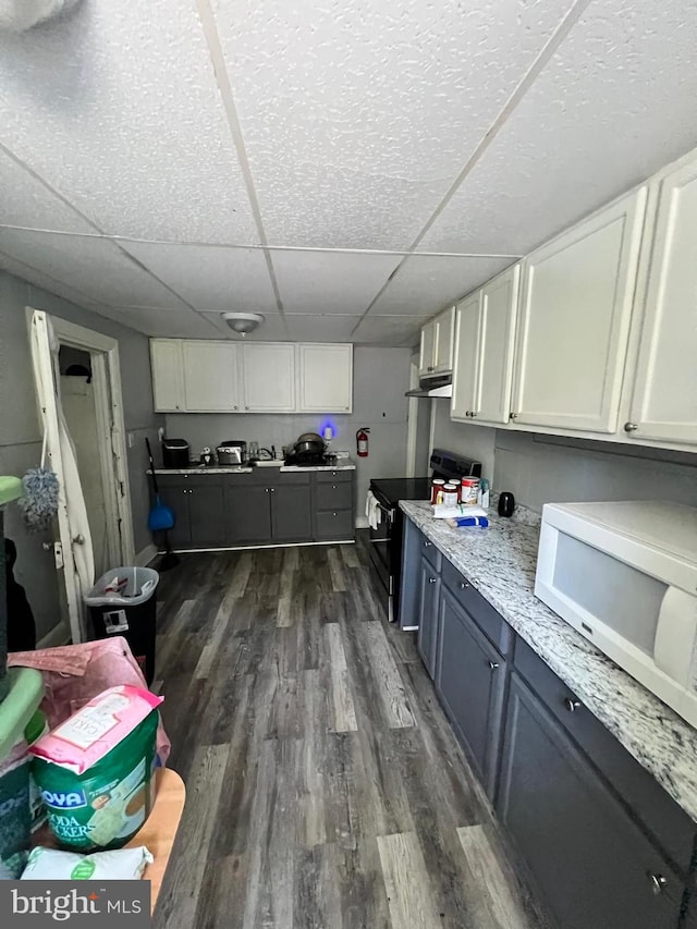 kitchen featuring a paneled ceiling, light stone counters, stainless steel electric range oven, dark hardwood / wood-style floors, and white cabinetry