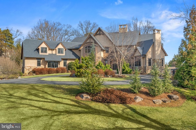 view of front of property featuring stone siding, a chimney, stucco siding, and a front yard