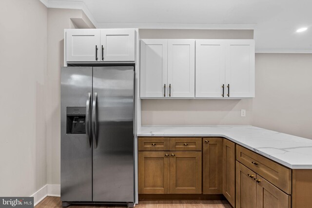 kitchen with light stone counters, stainless steel fridge, ornamental molding, light hardwood / wood-style flooring, and white cabinetry