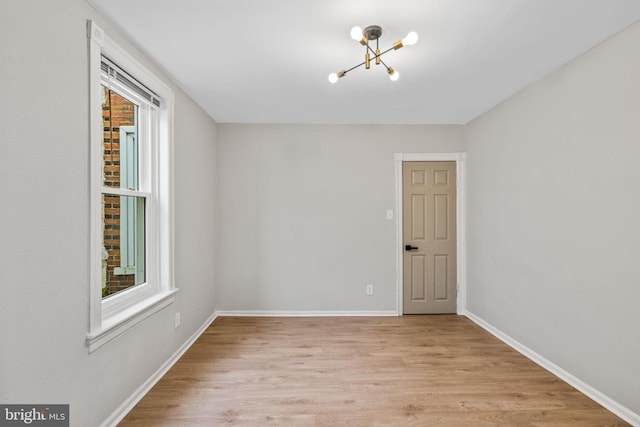 spare room featuring a healthy amount of sunlight, a chandelier, and light hardwood / wood-style floors