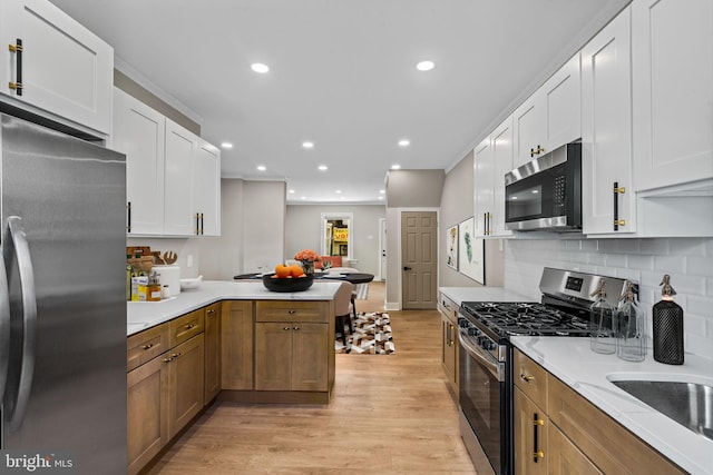 kitchen featuring decorative backsplash, white cabinets, kitchen peninsula, light hardwood / wood-style flooring, and appliances with stainless steel finishes