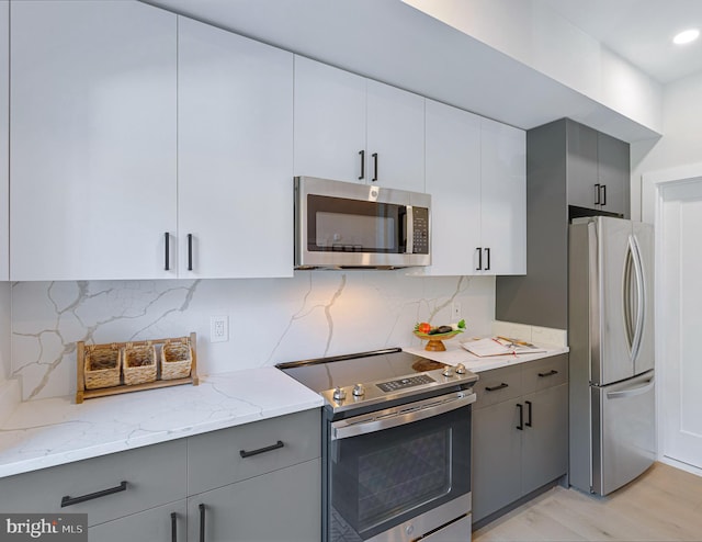 kitchen with light hardwood / wood-style floors, gray cabinetry, light stone countertops, backsplash, and appliances with stainless steel finishes