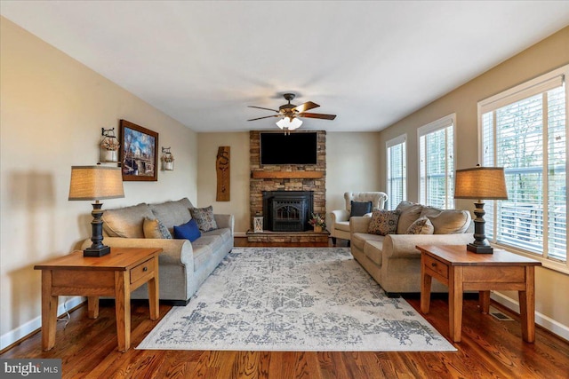 living room featuring ceiling fan, wood-type flooring, and a stone fireplace