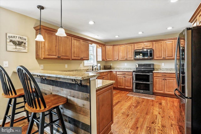 kitchen with stainless steel appliances, light hardwood / wood-style floors, kitchen peninsula, a kitchen breakfast bar, and light stone countertops