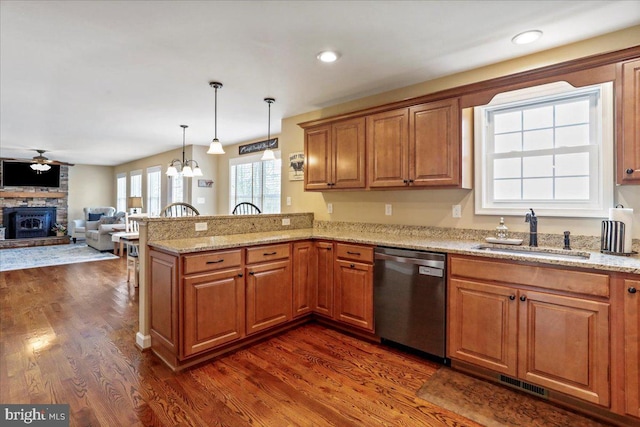 kitchen featuring sink, kitchen peninsula, stainless steel dishwasher, a stone fireplace, and dark hardwood / wood-style flooring