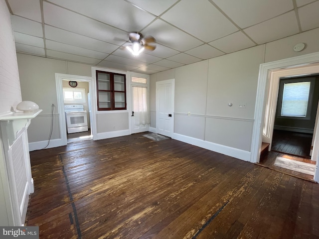 unfurnished living room with a drop ceiling, a wealth of natural light, ceiling fan, and dark hardwood / wood-style floors