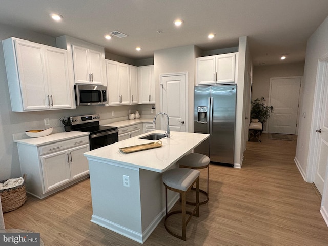 kitchen with a kitchen island with sink, white cabinetry, stainless steel appliances, and light hardwood / wood-style floors