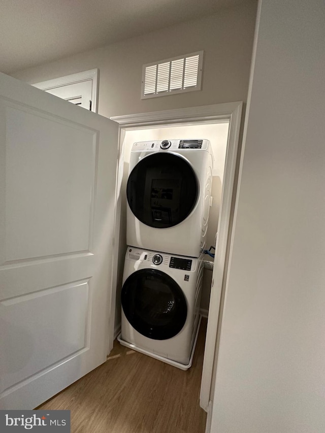 laundry room with hardwood / wood-style floors and stacked washing maching and dryer