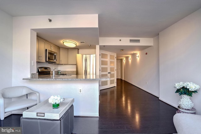 kitchen with kitchen peninsula, light stone countertops, appliances with stainless steel finishes, and dark hardwood / wood-style flooring