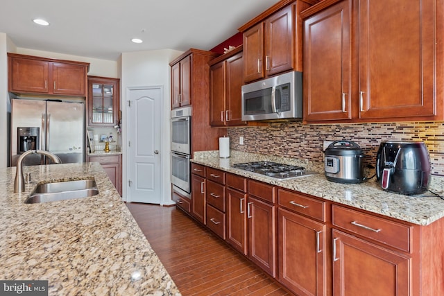 kitchen with backsplash, sink, light stone countertops, appliances with stainless steel finishes, and dark hardwood / wood-style flooring