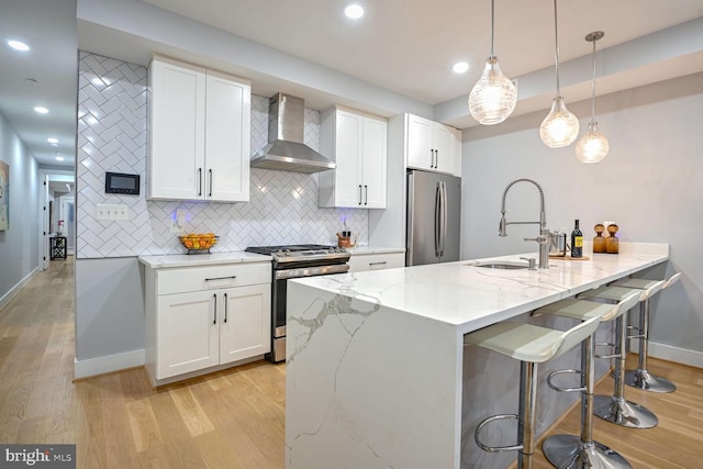 kitchen with pendant lighting, light hardwood / wood-style flooring, wall chimney range hood, white cabinetry, and appliances with stainless steel finishes