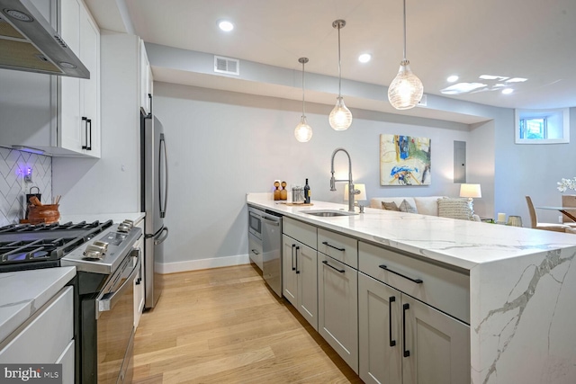 kitchen with extractor fan, light wood-type flooring, light stone countertops, backsplash, and appliances with stainless steel finishes