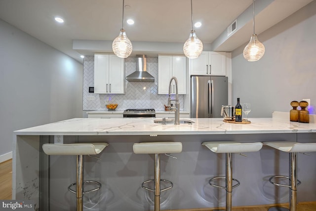 kitchen with white cabinets, sink, wall chimney range hood, hanging light fixtures, and appliances with stainless steel finishes