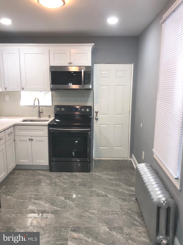 kitchen featuring tasteful backsplash, black range with electric stovetop, radiator, sink, and white cabinetry