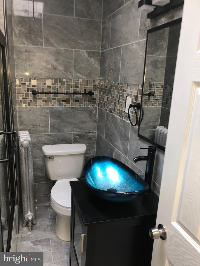 bathroom with vanity, toilet, radiator, and tile walls