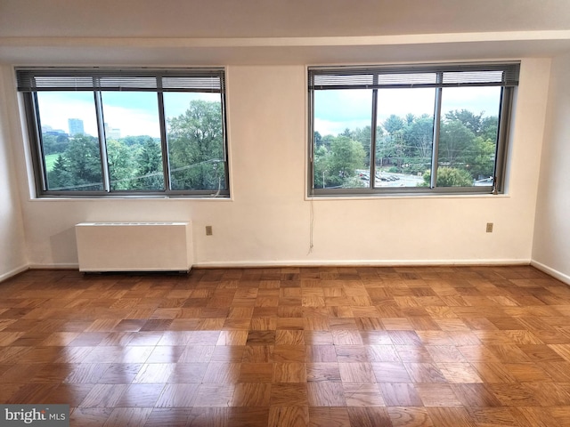 unfurnished room featuring radiator, parquet flooring, and a healthy amount of sunlight