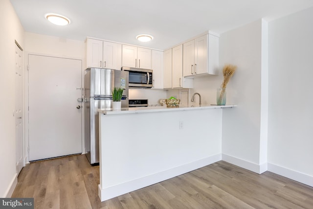 kitchen with appliances with stainless steel finishes, light hardwood / wood-style floors, kitchen peninsula, and white cabinetry