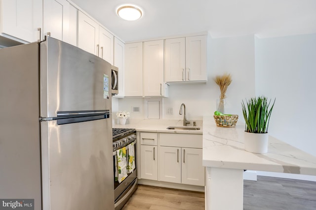 kitchen with sink, white cabinetry, stainless steel appliances, light stone countertops, and light hardwood / wood-style floors