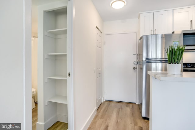 interior space with stove, stainless steel refrigerator, light wood-type flooring, and white cabinetry