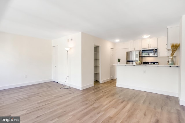 kitchen featuring stainless steel appliances, light wood-type flooring, kitchen peninsula, and white cabinetry