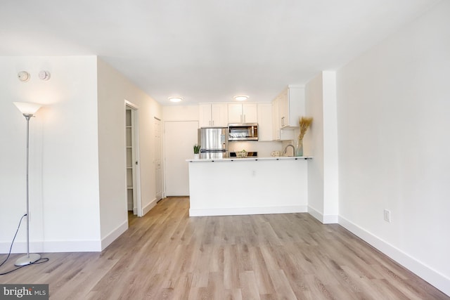 kitchen with stainless steel appliances, kitchen peninsula, light hardwood / wood-style flooring, and white cabinetry