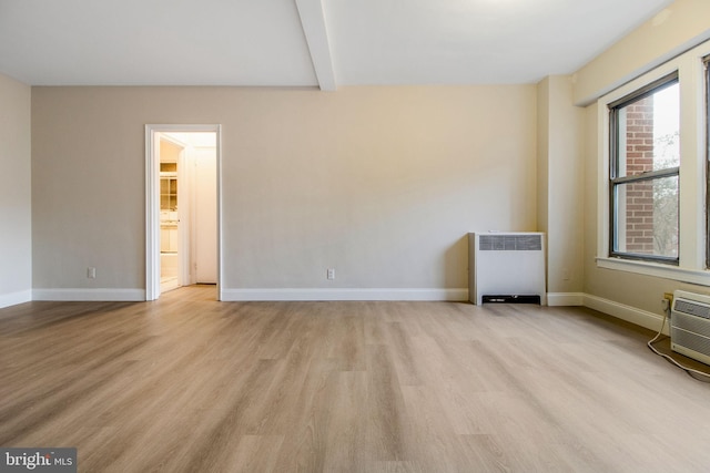 empty room featuring beam ceiling, radiator heating unit, and light hardwood / wood-style flooring