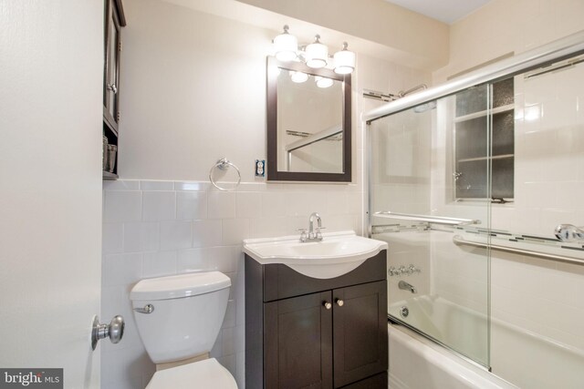 full bathroom featuring vanity, tile walls, toilet, and combined bath / shower with glass door