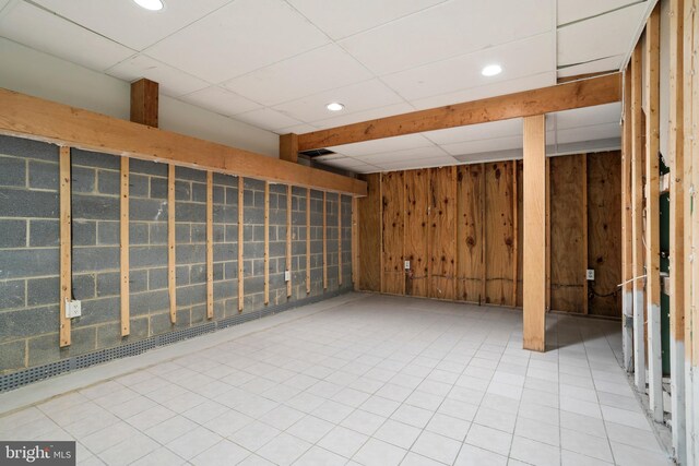 basement with a paneled ceiling, wood walls, and tile patterned floors