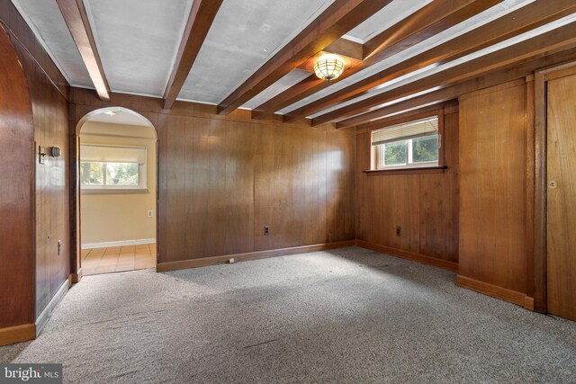 carpeted spare room with wood walls and beamed ceiling