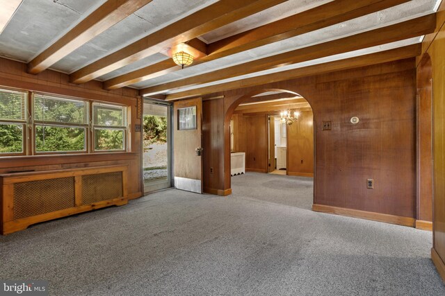 carpeted spare room with radiator, wood walls, and beam ceiling