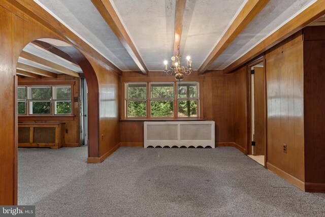 interior space with beam ceiling, a notable chandelier, wooden walls, and radiator