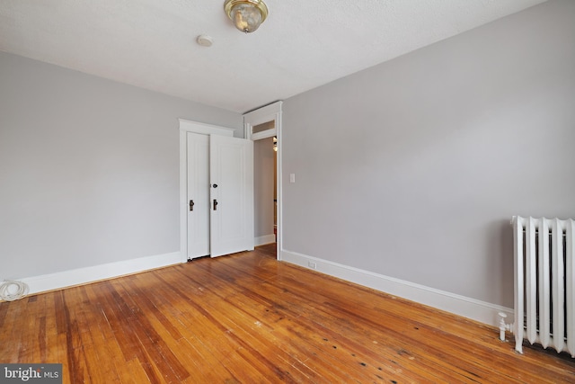 empty room featuring wood-type flooring and radiator heating unit