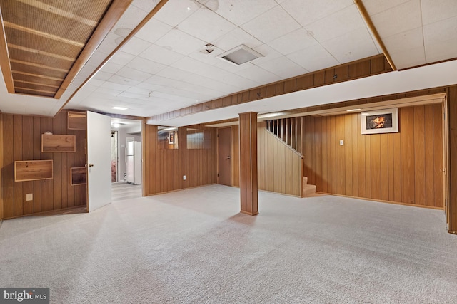 basement with white refrigerator, wooden walls, and light carpet