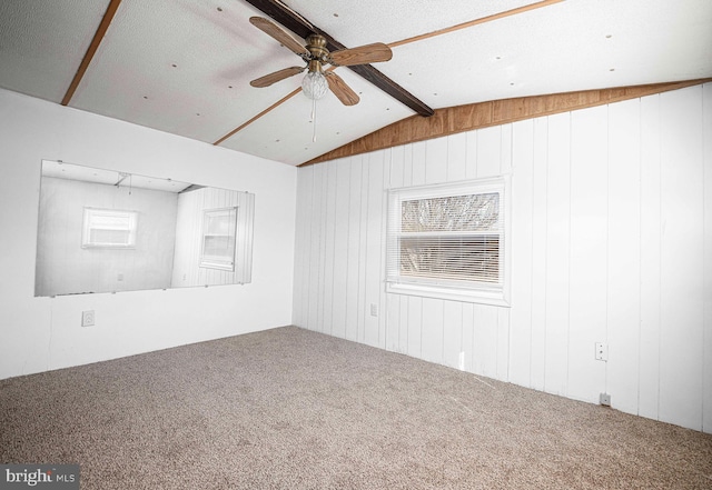 carpeted empty room with vaulted ceiling with beams, a textured ceiling, wooden walls, and ceiling fan