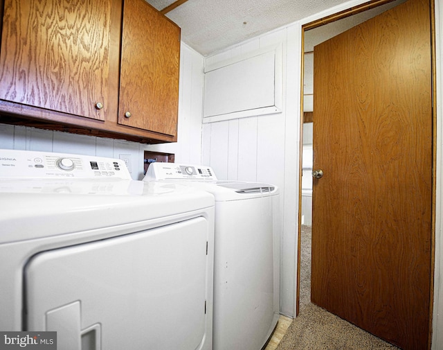 clothes washing area with wood walls, a textured ceiling, cabinets, and washing machine and clothes dryer