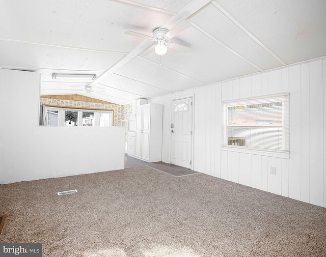 unfurnished living room with lofted ceiling, wood walls, and carpet flooring