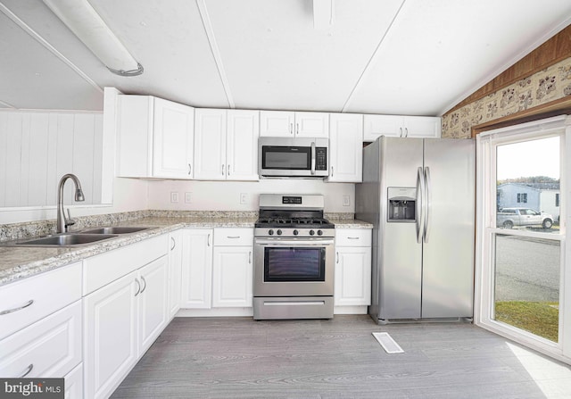 kitchen featuring lofted ceiling, stainless steel appliances, sink, white cabinets, and light hardwood / wood-style floors