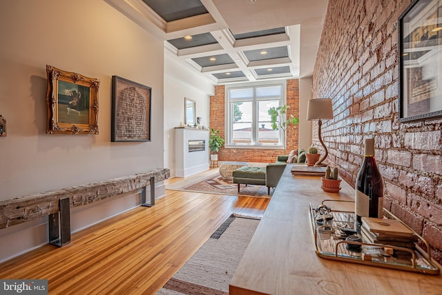 interior space featuring a brick fireplace, light wood-type flooring, coffered ceiling, beam ceiling, and brick wall