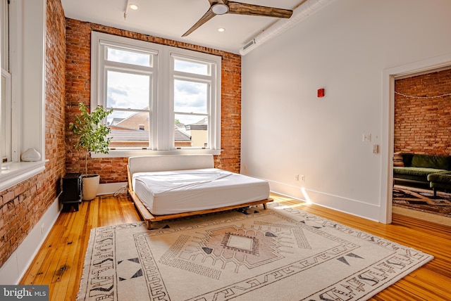 bedroom with wood-type flooring, brick wall, and ceiling fan