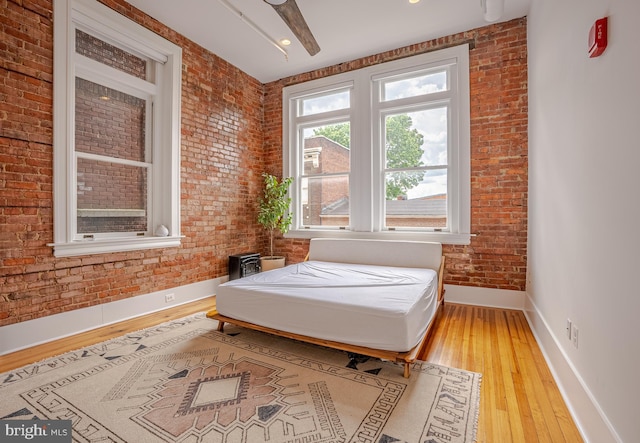 bedroom featuring brick wall, light hardwood / wood-style flooring, and ceiling fan