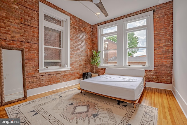 bedroom with ceiling fan, brick wall, and light hardwood / wood-style flooring