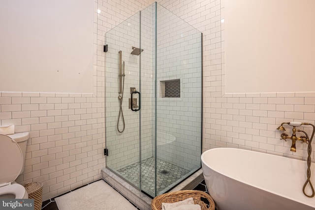 bathroom featuring separate shower and tub, toilet, and tile walls