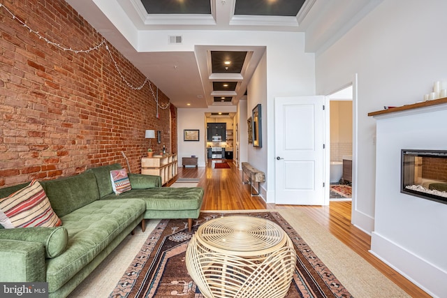 living room featuring brick wall, ornamental molding, hardwood / wood-style flooring, and a high ceiling