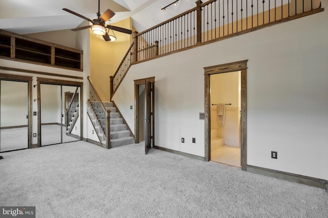 unfurnished living room with ceiling fan, high vaulted ceiling, and light carpet