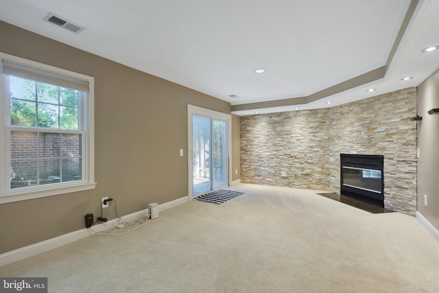 unfurnished living room with a stone fireplace, ornamental molding, and carpet flooring