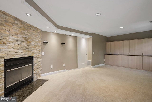 unfurnished living room featuring a stone fireplace and light colored carpet