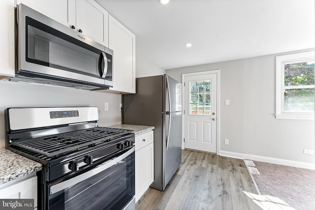 kitchen with appliances with stainless steel finishes, light hardwood / wood-style flooring, light stone counters, and white cabinetry